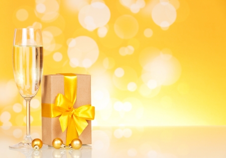 Glass with champagne and a gift on an abstract yellow backgroundの写真素材
