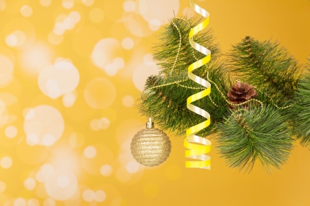 Branch of a Christmas fir-tree with ornament on an abstract yellow backgroundの写真素材