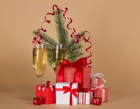 Fir-tree branch, wine glasses with champagne, big and small gift boxes on a beige backgroundの写真素材