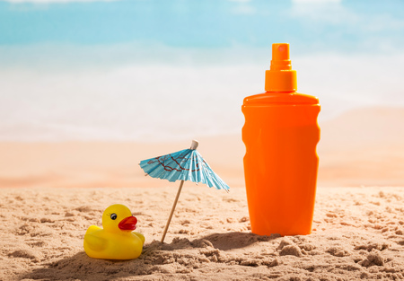 Sunscreen, umbrella and a rubber duck in the sand against the sea.の写真素材