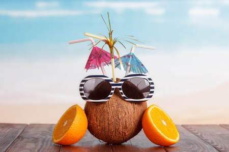 Coconut with straw, umbrellas, sunglasses and a part of orange on a brown table against the sea.の写真素材