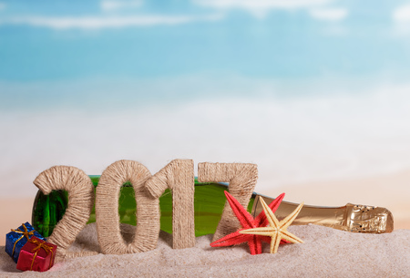 Figures 2017 and a bottle of champagne, sea stars, gifts in the sand against the sea.