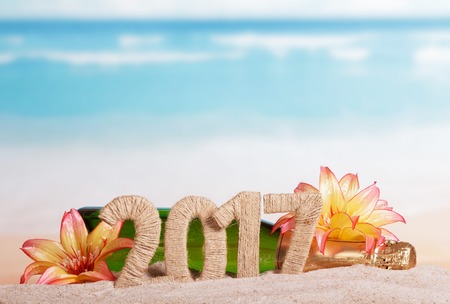 Figures 2017, a bottle of champagne and flowers in the sand against the sea.