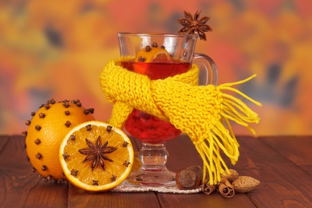 Mulled wine wrapped in a scarf, oranges and nuts on a background of autumn leaves.の写真素材