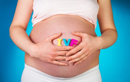 Pregnant woman holding hands in IVF lettering on a blue background.の写真素材