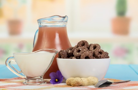 A jug of juice, a bowl of corn rings with cocoa and sesame, sour cream, peanuts on the background of the kitchen.の写真素材