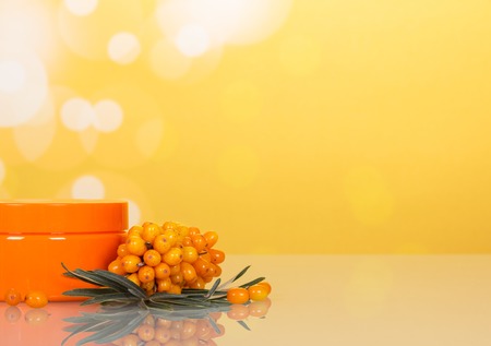 Bunch of sea buckthorn and jar with cream on an abstract yellow background.の写真素材