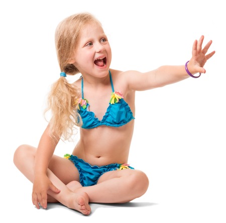 Seated petite blond girl in a swimsuit, her arm stretched forward isolated on white background.の写真素材