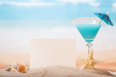 Blank card, cocktail, seashells and starfish in the sand against the sea.の写真素材