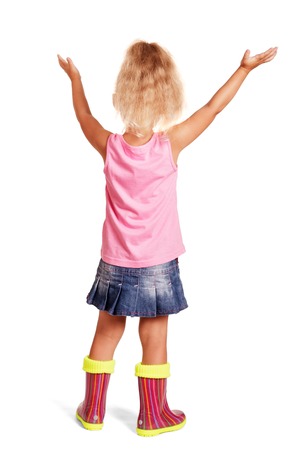 Little blond girl in a blouse, a skirt and rubber boots with her hands raised standing isolated on white background. Back view.の写真素材