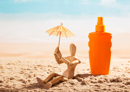 Sunscreen and a wooden doll with umbrella on the seashore.の写真素材