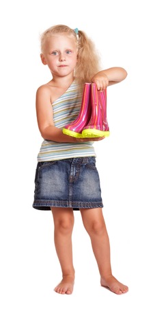 Little blond girl in a skirt and blouse standing and holding a rubber boots isolated on white background.の写真素材