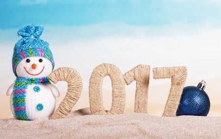 The inscription 2017 in the sand, a snowman, a Christmas ball on the background of the oceanの写真素材