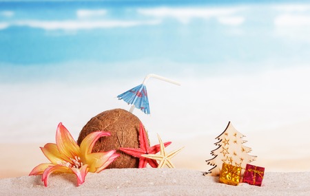 Christmas accessories in the sand, coconut, tree, presents on background of oceanの写真素材