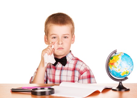 Sad boy sits at a table with a notebook and globe isolated on white background.の写真素材