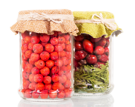 Jars with rowan berries and rose hips isolated on a white background.の写真素材