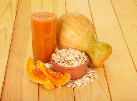 Pumpkin seed bowl and glass of juice on a background of light wood.の写真素材