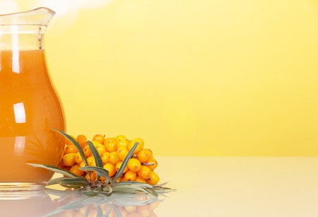 A jug of juice from the berries of sea buckthorn on abstract yellow background.の写真素材