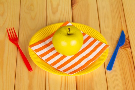 Bright disposable tableware, napkin and apple on a background of light wood. View from above.の写真素材