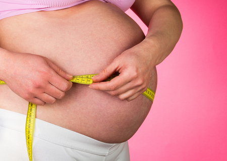 Pregnant woman measuring her belly on a pink background.