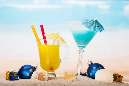 Juice cocktail starfish, seashells, christmas balls and gifts in the sand against the sea.の写真素材