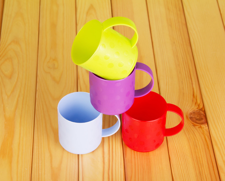 Four different color plastic mugs on the background of light wood.の写真素材