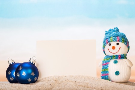 Blank white postcard, snowman and Christmas balls in the sand on the seashore.の写真素材