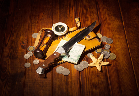 Accessories for the traveler: the compass, an hourglass, knife and money on a background of dark wood.の写真素材