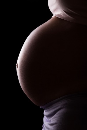 A pregnant woman in profile isolated on a black background.