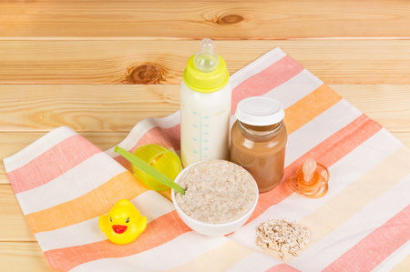 A bottle of milk, a bowl of oatmeal, mashed potatoes, nipple and rubber duck on a background of light wood.の写真素材
