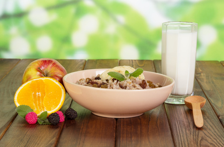 A bowl of oatmeal with raisins, cup of yogurt and fruit on abstract green background.の写真素材