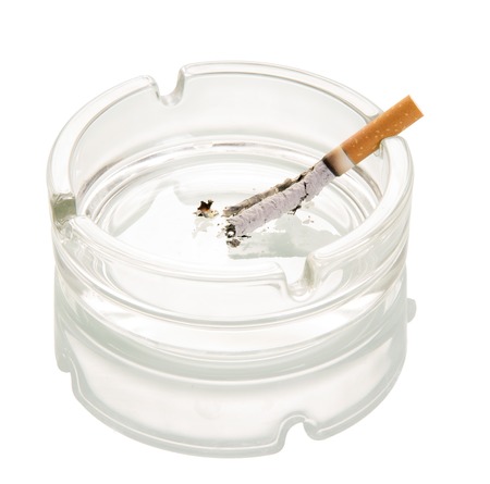 Decaying cigarette in a glass ashtray isolated on white background.の写真素材