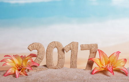 Christmas inscription 2017 in the sand decorated with tropical flowers on a background of the seaの写真素材