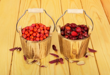 Buckets filled with rosehip and rowan berries on a background of light wood.の写真素材