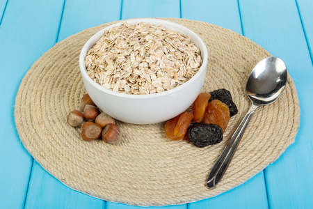 In a white bowl, oatmeal, nuts and dried fruits on a background of wooden planks painted in blue color.の写真素材