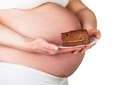 Pregnant woman holding a piece of cake isolated on white backgroundの写真素材