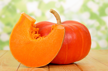 Round, orange pumpkin and cut a piece on an abstract green background.の写真素材