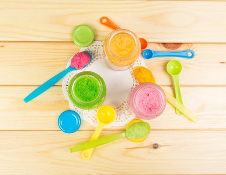 Baby puree in a spoon and open banks against the backdrop of pale wood.の写真素材
