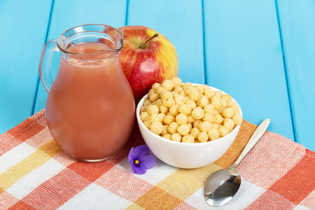 Apple juice in a jug and corn balls into a bowl on a wooden background okreshennogo blue.の写真素材