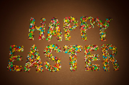 Inscription Happy Easter, lined with colorful granules of sugar confetti on a brown background.の写真素材