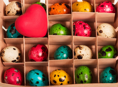 Colored Easter eggs in a box with cells and red heart. Background.の写真素材