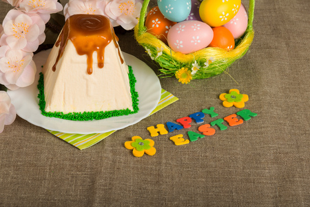 Colored Easter eggs in the basket, traditional Easter cheesecake dessert watered icing inscription Happy Easter and a branch with flowers on sackcloth. Background.の写真素材