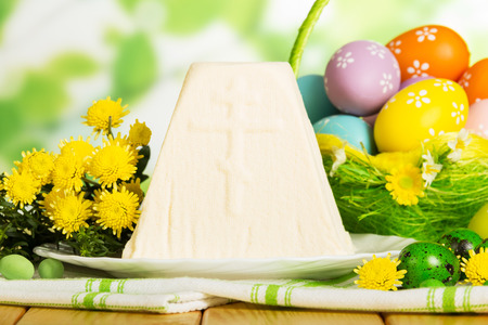 Colored Easter eggs in the basket, traditional Easter cheesecake dessert on a cloth, herbs, candies on abstract green background. Close-up.の写真素材