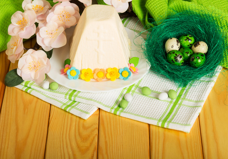 Easter eggs in the nest, a traditional Easter cheese dessert on a plate decorated with flowers, branch with flowers, candy and cotton towels. Background.の写真素材