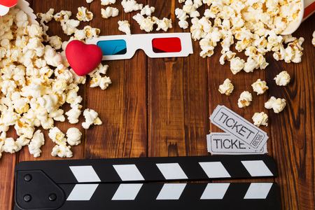 Lots of popcorn, 3D-glasses, red heart, movie tickets and movie clapper against the dark wood.の写真素材