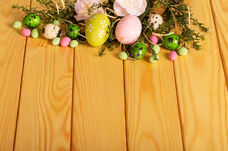 Colored Easter eggs, branch with flowers, candy and grass on a background of light wood.の写真素材