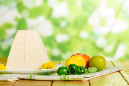 Traditional Easter cheese dessert, colored Easter eggs, flowers on a fabric napkin. Abstract green background.の写真素材