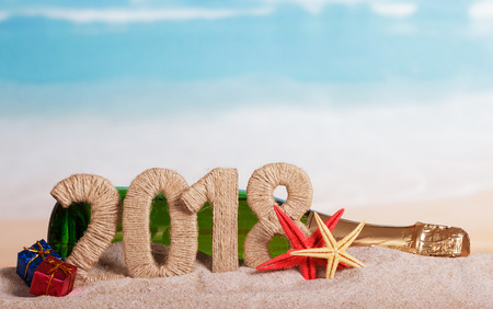New Year inscription 2018, a bottle of champagne, gifts and starfish in the sand on the beach.の写真素材