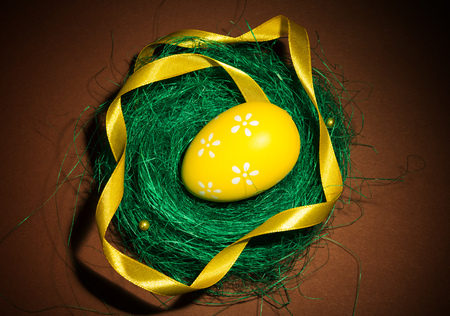 The nest, lined with grass Easter egg and ribbon on a brown background.の写真素材