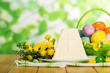 Colored Easter eggs in the basket, traditional Easter dessert cheese cloth napkin, flowers, candies on abstract green background.の写真素材